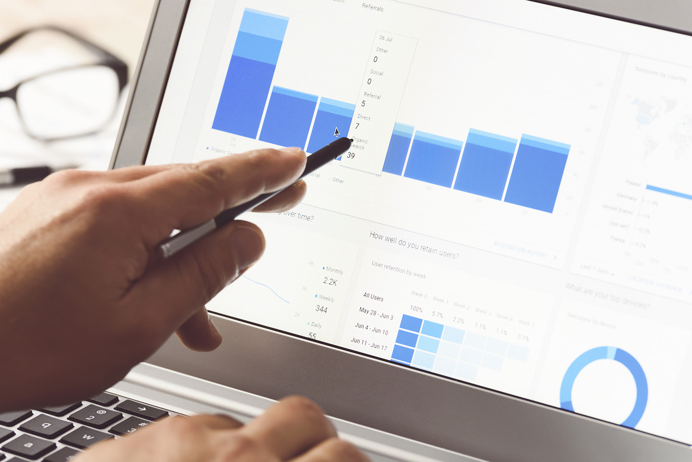 A person points at a bar graph on a laptop screen displaying analytics data, suggesting analysis of business or website performance and exploring questions like how long does SEO take. Glasses are visible in the background.